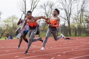 Indiana Tech relay team passing a baton in a race on the outdoor track